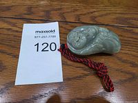 Top view of green carved jade pendant showing floral and abstract designs and the attached red braided cord with bead.