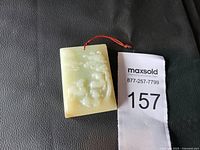 Front side of rectangular carved jade pendant showing detailed floral and fruit motifs with a red hanging cord.