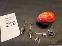 Overview of the pair of brass-tone dangle earrings, polished red stone egg, and four silver-tone animal charms on dark surface.