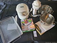 Full lot overview showing all kitchen items including the Philips Party Master Kit, rice cooker, coffee maker, two steam pots, kitchen scale, and wire basket rack arranged on a black surface.