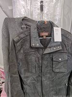 Photo shows a dark gray men's genuine leather jacket by Danier with zippered pockets and snap button collar, hanging on a rack next to a gray knit sweater.