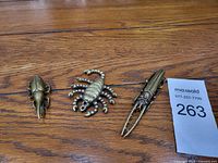 Front view of three metal insect figurines on a wooden surface with auction lot number 263 visible