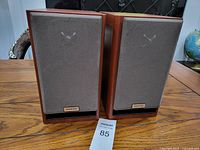 Pair of Onkyo bookshelf speakers front view showing wood veneer sides and brown fabric speaker covers with Onkyo logos.