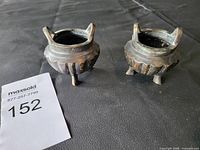 Pair of small vintage bronze incense burners photographed showing tops and handles on a black surface.