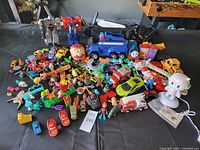 Wide view of the toy collection, showing a large number of small toys, vehicles, and some electronic toys on a black surface.