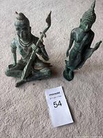 Photo showing both bronze figures on a soft gray surface with auction lot tag 54.