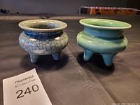 Two vintage ceramic urns shown from side angle on a black surface with lot number card 240 visible.