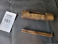 Photo showing the brass lock body and detachable bar placed on a dark surface next to a lot number card