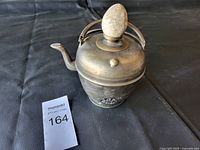 Full view of the vintage brass tea pot with stone egg finial, showing shape, handle, spout, and patina.