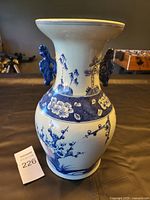 Front view of the porcelain vase showing floral patterns, figures, and blue crafted handles.