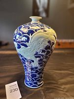 Front view of vintage vase showing the curved body decorated with detailed blue wave designs and a prominent raised dragon in white relief.