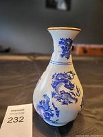 Front view of vintage white porcelain vase with blue dragon design and gold trim on rim