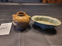 Photo showing front view of brown floral relief vase next to pale green scalloped edge bowl on black surface.