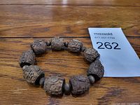 Wooden bracelet made of large cylindrical carved wooden beads with smaller round spacers, arranged in a circle on a wooden surface.