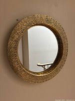 Front view of round 18-inch mirror showing detailed ornate gold-tone metal frame with floral and circular embossed patterns