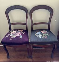 Front view of two Victorian needlepoint chairs showing floral upholstery in two different colors on wooden frames.