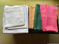 Top-down view of folded white, beige, green, and pink floral embossed tablecloths showing texture and scalloped edges