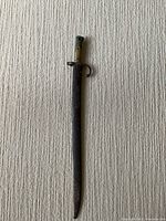 Full length photo of bayonet in scabbard on a textured carpeted surface.