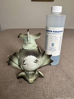 Photo of a dragon-shaped light green candle holder and a 500ml bottle of liquid paraffin labeled 'Liquid Paraffin Extra Pure 1L'