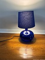 Photo of cobalt blue glass table lamp on wooden surface, showing power cord and light cast on floor.