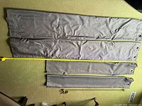 Four gray curtain panels laid flat on floor showing length with measuring tape and metal grommets for top hanging.