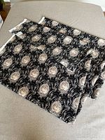 Folded black and beige Versailles pattern fabric with detailed ornate motifs shown on a neutral surface.
