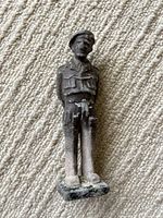 Full view of the lead figurine standing on carpet, showing front and side details of uniform and cap, with aging wear and patina.