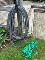 Two garden hoses coiled on a wooden holder next to a patio: a thick black hose and a green soaker hose with tape.