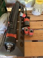 Two Gardena oscillating sprinklers and three hose connectors on wooden bench