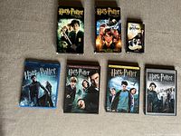 Collection arranged on a flat surface including three DVD cases, three VHS tapes, and a small box of playing cards, all Harry Potter themed.