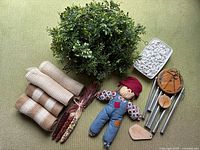 Five artificial eucalyptus garlands arranged in a pile with mesh ribbon rolls, white decorative stones, small scarecrow doll, decorative corn, and Weatherland wind chime