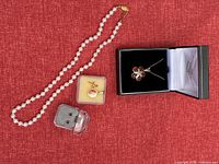 Full set of jewelry items on red background including silver chain with amber flower pendant, earrings, cross pendant in box, pearl-like necklace, and gold-tone chain with pendant.