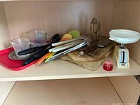 Overview of assorted kitchenware items showing spatulas, tongs, measuring cups, trays, cutting boards, scale