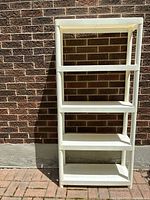 Full view of white plastic shelving unit with five shelves against brick wall. Shows overall size and condition.
