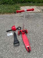 Image of red 3-in-1 children's scooter parts including scooter base with adjustable handlebar, red detachable seat, black handle, and assembly screws on pavement.