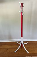 Full view of the red and white metal coat rack showing four legs and four hooks on a red post.