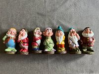 Front view of the seven dwarf plastic figurines lined up side by side on a fabric surface.