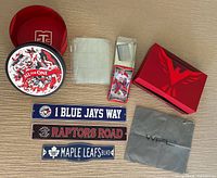 Photo showing set of sports memorabilia including collectible hockey card tin, three metal street signs for Blue Jays, Raptors, and Maple Leafs, two card holders with hockey cards, red storage box with winged logo, and gray cloth bag with WPL branding.