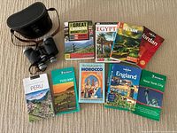 Full lot with travel guidebooks and binoculars with carrying case on carpet background