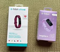 Both Fitbit boxes side by side: Fitbit Alta HR box with fuchsia band image, Fitbit Inspire 3 box with light purple tracker image