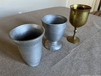 Three vintage goblets including one brass chalice and two metal goblets displayed on a table showing height and condition