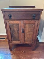 Front view of vintage wooden cabinet showing drawer and double doors with metal hardware and visible wear.