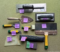 Photo showing various drywall and wall repair tools laid out on carpet with pink labels identifying each tool.