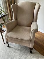 Front view of beige textured checkered wingback chair showing seat cushion, armrests, winged back, and wooden cabriole legs.
