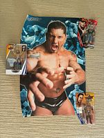 Three WWE action figures: John Cena, The Rock, and Elite Collection figure in original packaging, displayed with a Batista poster.