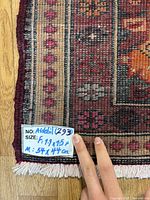 Close-up photo of rug label showing size and lot number, with fingers for scale. Rug size given as 1.9 x 1.5 ft (54 x 44 cm). Wool on cotton weave visible.