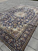 Full view of navy background rug with central medallion and floral border laid on stone floor