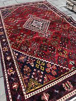 Front view of red Joshaghan rug laid on stone floor showing overall pattern and central medallion.