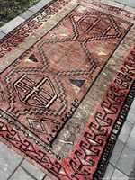 Full view of rectangular Persian Lori rug laid out on stone floor showing geometric pattern in earth tones, low pile wool texture.