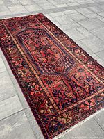 Full view of rug laid flat on stone floor showing central medallion and border pattern